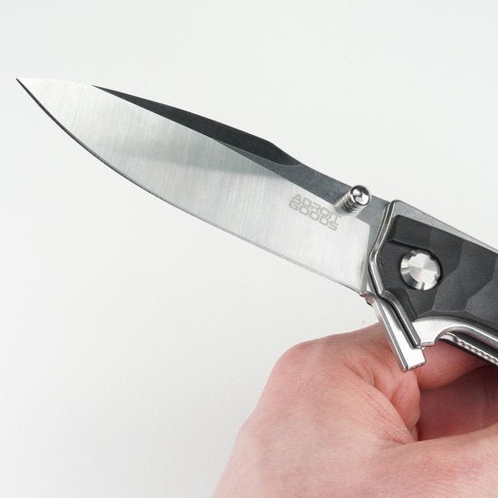 Hand met een opengevouwen scherp mes met metalen lemmet en zwart handvat tegen een witte achtergrond