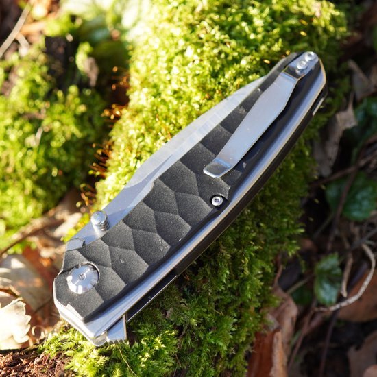 Gesloten zakmes met zwarte, getextureerde handgreep liggend op groene mosbodem buiten.