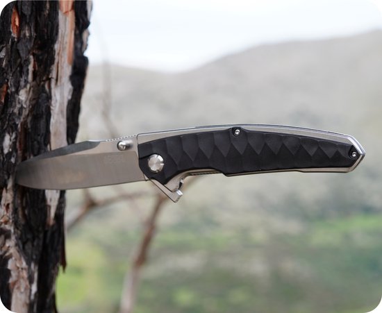 Zakmes met zwart handvat in de bast van een boom, natuur op de achtergrond