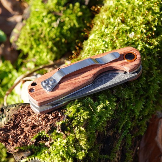 Opgevouwen zakmes met houten handvat en metalen clip liggend op groene mosbedekking