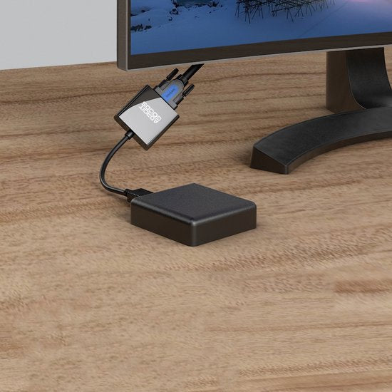 Zwarte kleine adapter met aansluitkabels naast een computerscherm op een houten bureau