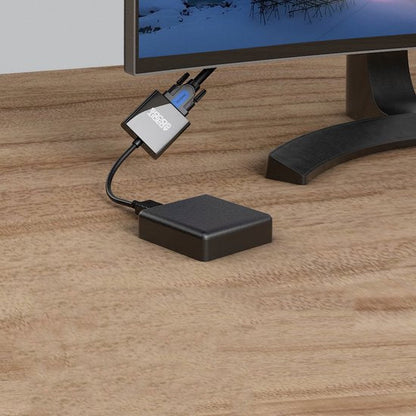 Zwarte kleine adapter met aansluitkabels naast een computerscherm op een houten bureau