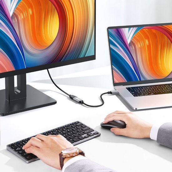 Handen bedienen toetsenbord en muis verbonden met laptop en extern scherm met kleurrijk beeld