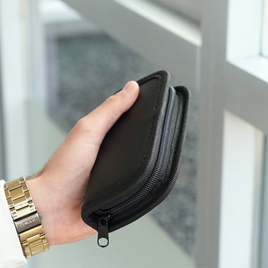 Hand die een compact zwart etui met ritssluiting vasthoudt in lichte omgeving bij raam