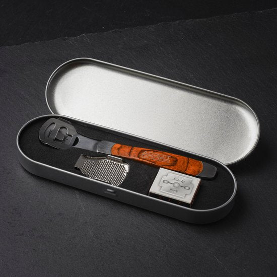 Metalen opbergdoosje met een zwarte scheermes en een doosje vervangende mesjes op zwarte achtergrond