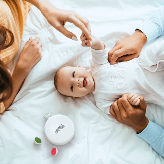 Vrolijke baby ligt op bed terwijl ouders liefdevol handen vasthouden en zachte pillendoos naast hen ligt