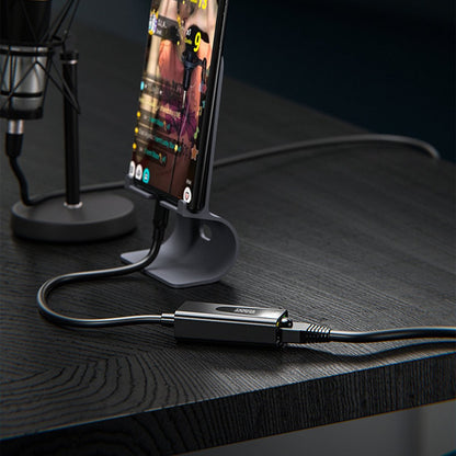 Smartphone op een standaard met aangesloten adapter en kabels op een donker houten tafelblad.