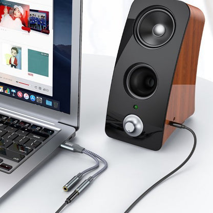 Laptop verbonden met een houten speaker en een adapterkabel voor audio-uitbreiding.