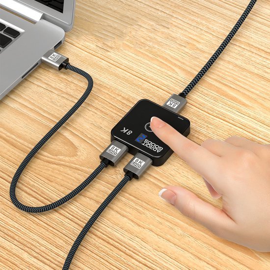 Hand bedient kleine zwarte mediasplitter met aansluitingen op houten bureau naast laptop