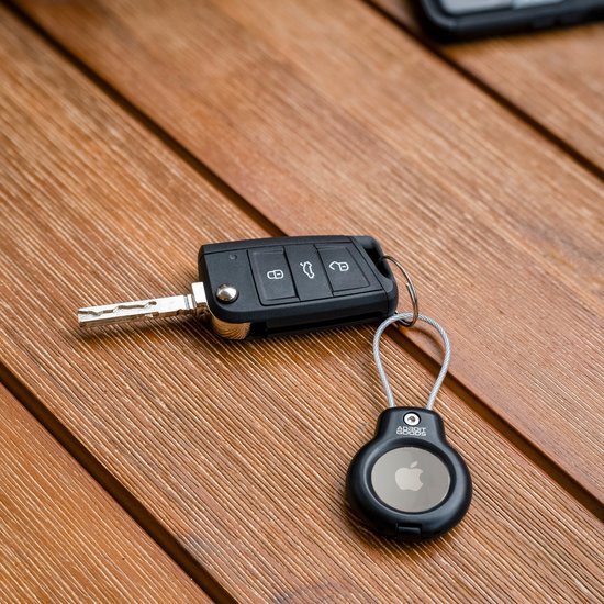 Autosleutel met sleutelhanger en klein zwart Apple AirTag apparaatje op houten tafel