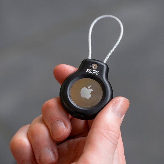 Hand houdt zwart beschermhoesje met een draadlus voor een ronde Apple tracker.