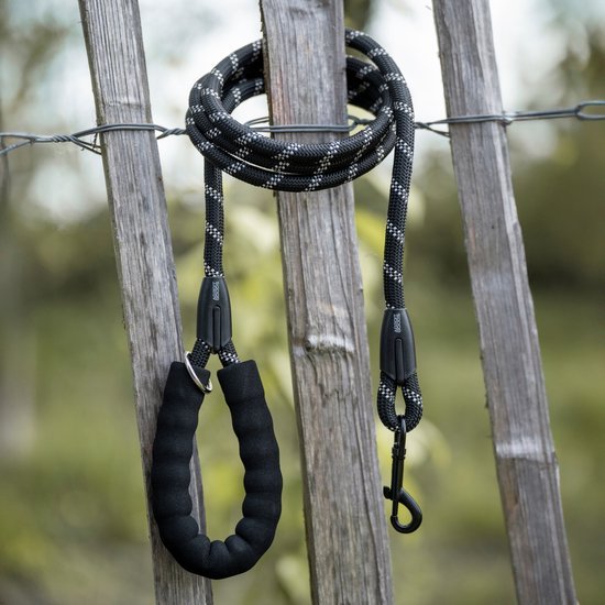 Zwarte hondenriem met lus en metalen haak hangt aan houten hekwerk buiten.
