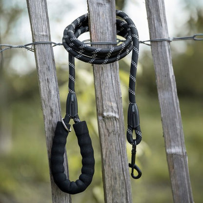 Zwarte hondenriem met lus en metalen haak hangt aan houten hekwerk buiten.