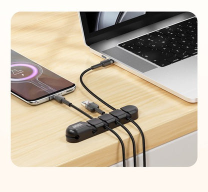 Zwarte kabelorganizer op houten bureau met meerdere aangesloten oplaadkabels bij laptop en smartphone.