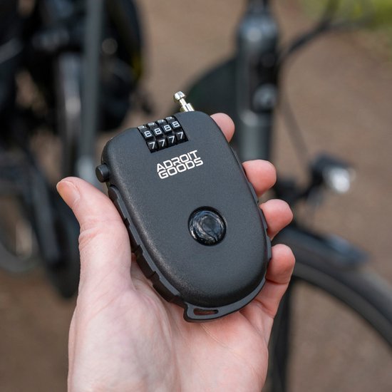 Hand die een zwart compact cijferslot met AdroitGoods logo vasthoudt bij een fiets buiten