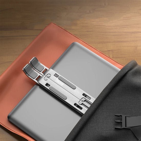 Close-up van een stijlvol grijs laptopstandaard op een houten tafel naast een oranje hoes en zwarte tas.