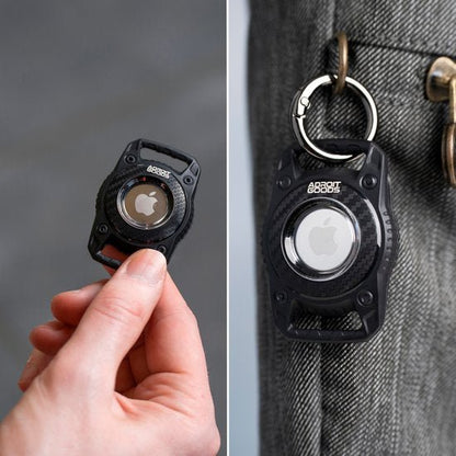 Hand houdt zwarte houder met wit Apple-logo, bevestigd aan jeans met sleutelhangerclip