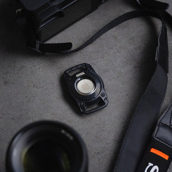 Zwart cameraaccessoire met band en lens op een grijze ondergrond, professioneel ogend