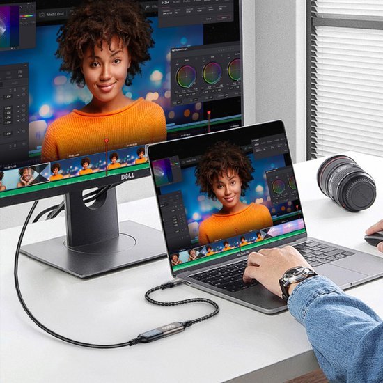 Person die videobewerking doet op laptop en externe monitor met kleurcorrectieschermen zichtbaar