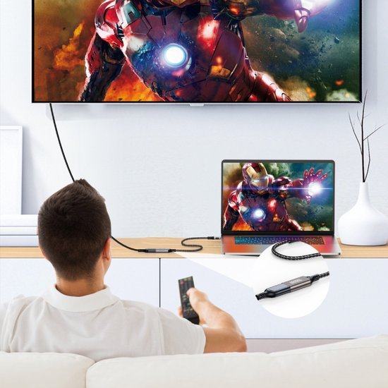 Man kijkt naar scherm met superheldenfilm, laptop verbonden met grote tv via kabeladapter.