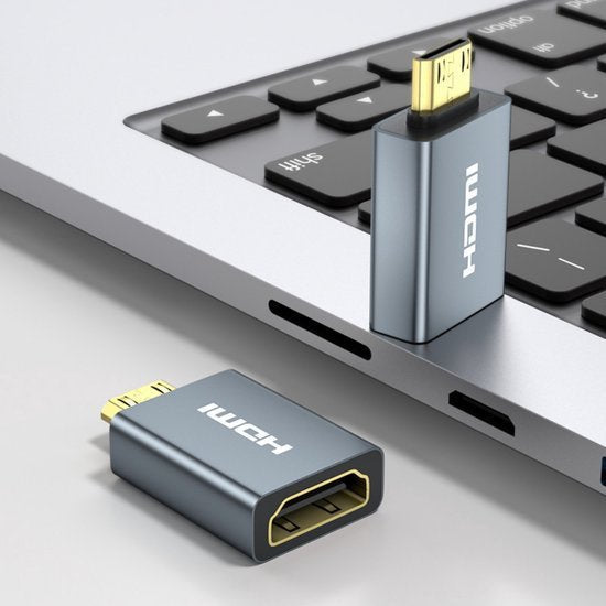Grijze micro HDMI naar standaard HDMI adapter naast laptop met één adapter in USB-poort geplaatst