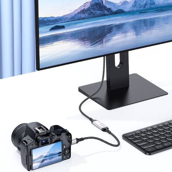 Digitale camera verbonden met een monitor en toetsenbord via een USB-kabel op een witte tafel.