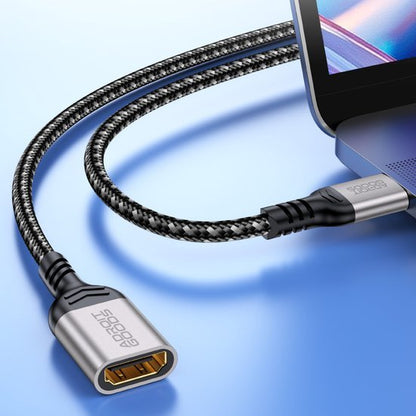 gevlochten adapterkabel aangesloten op laptop met metalen behuizing in neutrale achtergrond