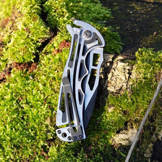 Inklapbaar metalen zakmes met futuristisch ontwerp ligt op mos en hout in de natuur.