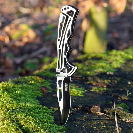 Zilverkleurig inklapbaar mes met zwart lemmet, staand in mosrijke bosgrond.