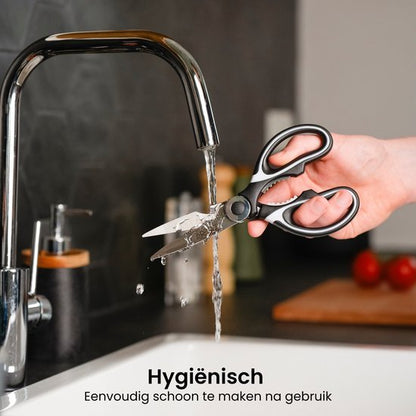 Hand houdt zwarte keukenschaar onder stromend water bij een roestvrijstalen kraan in keuken