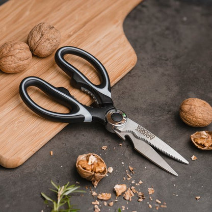 Zwarte keuken schaar met notenkraker en walnoten op houten plank en stenen ondergrond