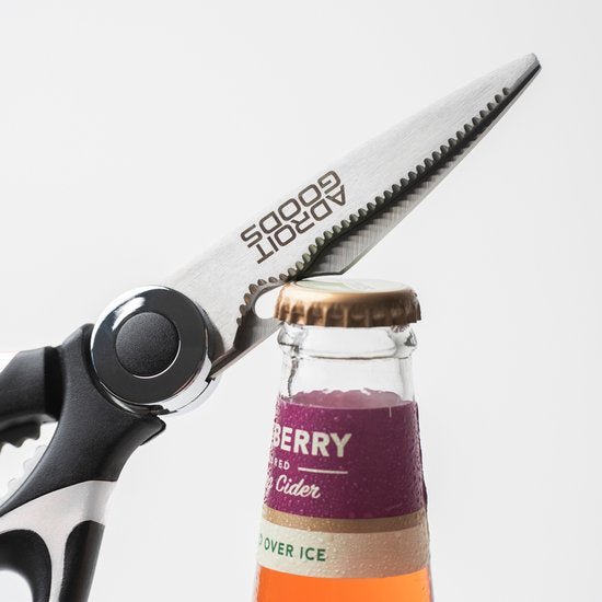 Schaar met kartelblad opent kroonkurk van flesje op een lichte achtergrond