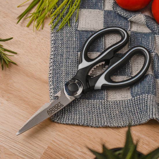 zwarte en grijze keukenschaar met gekarteld lemmet op blauwe doek bij kruiden en tomaten