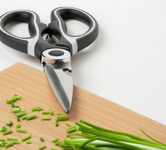 keukenschaar met zwarte kunststof handgrepen en gesneden groene kruiden op houten snijplank