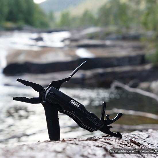 Zwarte multifunctionele tool met tang en andere functies, geplaatst op rots bij water stroomgebied.