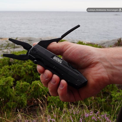 Hand houdt zwarte multifunctionele tang met AdroitGoods logo in natuurlijke buitenomgeving