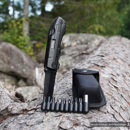 Zakmes met verschillende bitjes en zwarte draagtas op boomstam in buitenomgeving