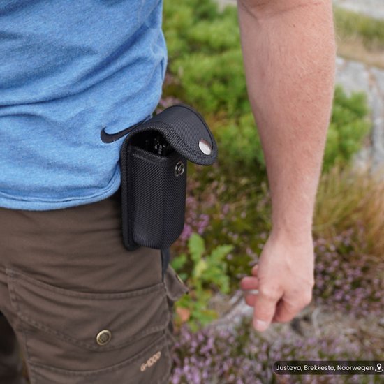 Persoon draagt een zwarte draagbare tas bevestigd aan een riem buiten in de natuuromgeving