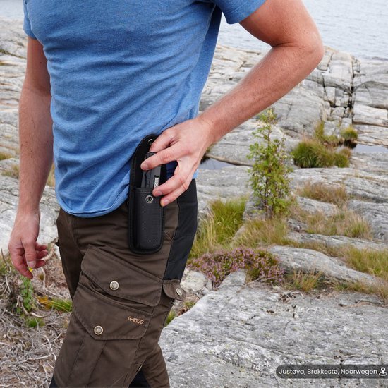 Man die een klein zwart etui uit een broekzak haalt in een buitenomgeving met rotsen en gras