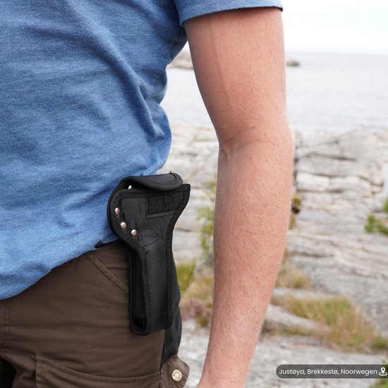 Man draagt een zwart holster aan zijn heup bij een rotsachtige kustlijn buiten.