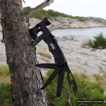 Zwart multitool met zaag, mes en hamer bevestigd aan een boom in natuurgebied.