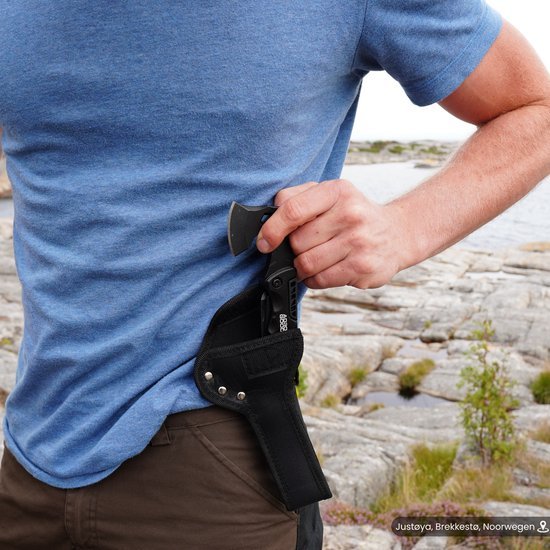 Man in blauw T-shirt stopt zwart holster met klein stuk gereedschap of mes in zijn broek aan rotsachtige kustlijn