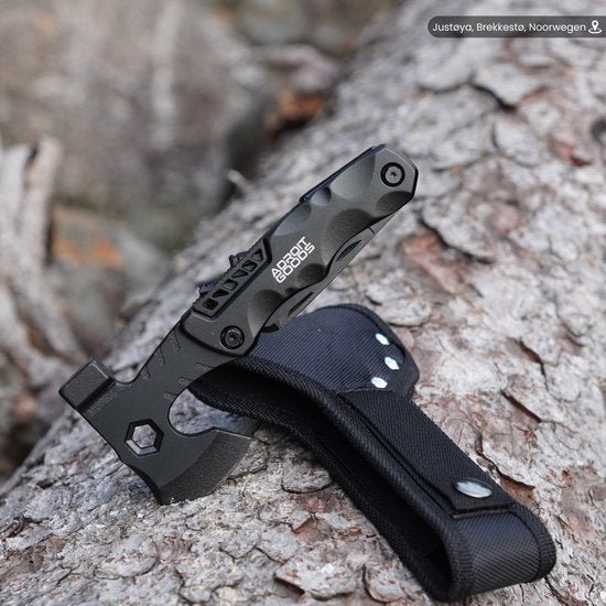 Zwart robuust multitool mes met hoes, geplaatst op boomschors in buitenomgeving.