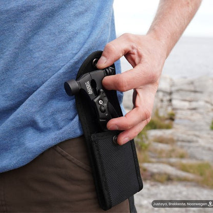 Mannelijke hand die een zwart multitool in een textielen hoes aan een broekriem steekt bij buitenlocatie