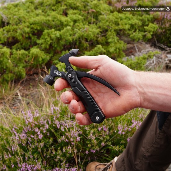 Hand houdt een compact zwart multitool gereedschap in een natuurlijke buitenomgeving