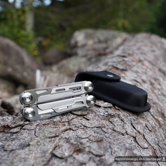 Multitool van roestvrij staal met zwarte draagtas, geplaatst op boomschors in de natuur