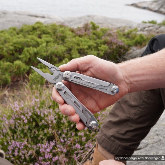 Hand die multifunctionele tang met grip in een natuurlijke buitenomgeving vasthoudt.