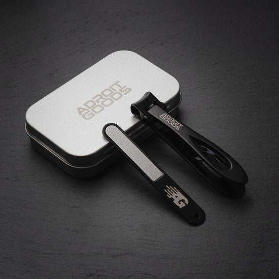 Zwarte nagelknipper en vijl met logo in metalen opbergdoos op donkere ondergrond