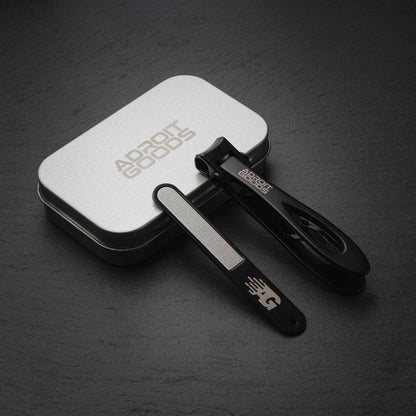 Zwarte nagelknipper en vijl met logo in metalen opbergdoos op donkere ondergrond