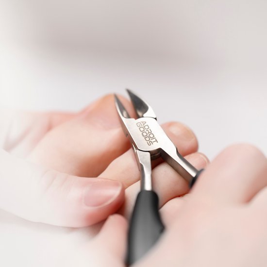 Close-up van vingers die scherpe metalen nagelknipper met zwarte handvatten vasthouden.